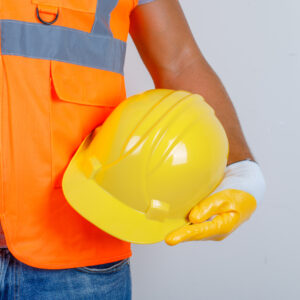 Male builder in uniform, jeans, gloves holding helmet in his hand , front view.